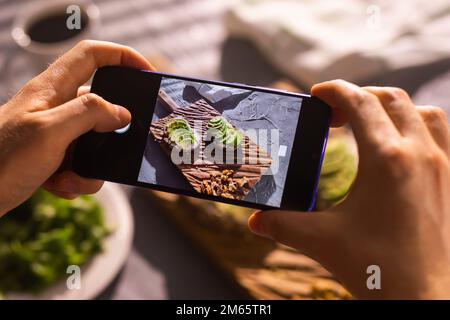 Smartphone prenant des photos de sandwichs biologiques sains avec de l'avocat. Main d'homme. Banque D'Images