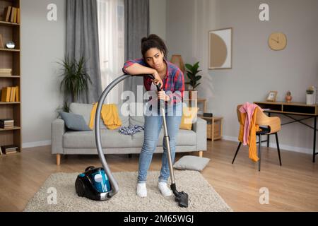 Une femme au foyer afro-américaine triste et délabrée du millénaire se repose sur un aspirateur Banque D'Images