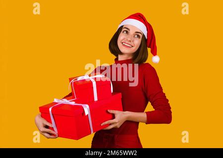 Bonne jeune femme en chapeau de père Noël tenant des cadeaux de Noël Banque D'Images