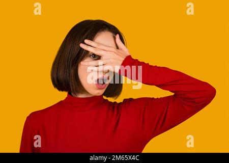 Belle jeune femme portant un chandail rouge décontracté peeking dans le choc Banque D'Images