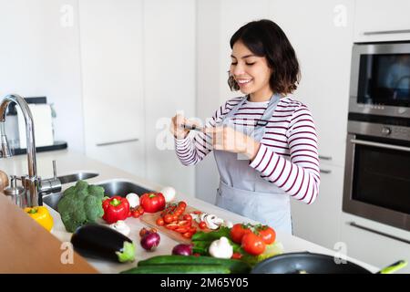 Femme hispanique prenant des photos avec le téléphone tout en cuisinant dans la cuisine Banque D'Images