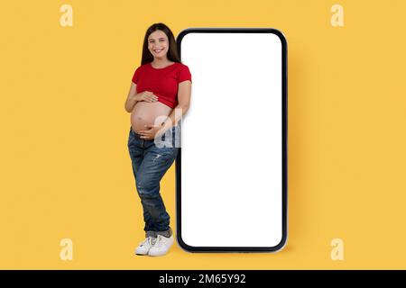 Maquette mobile. Souriante jeune femme enceinte penchée au smartphone Big Blank Banque D'Images