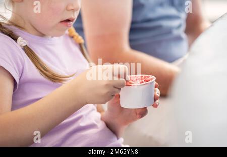 Anonyme école primaire enfant fille manger de la crème glacée d'une petite tasse blanche en papier vierge avec une cuillère, gros plan, détail, une personne. Les enfants mangent Banque D'Images