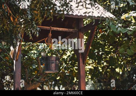 Un puits d'eau en bois à l'ancienne avec un seau en métal d'acier attaché à une longueur de corde Banque D'Images