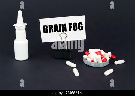 Concept médical. Sur la surface noire d'une pilule, un spray nasal et une carte de visite sur un trombone de bureau avec l'inscription - Brain FOG Banque D'Images