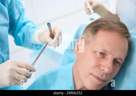 Homme d'âge moyen assis et en attente de points de suture médicaux Banque D'Images