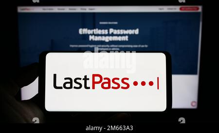 Personne tenant un téléphone portable avec le logo de la société de gestion de mot de passe LastPass US LP à l'écran en face de la page Web d'affaires. Mise au point sur l'affichage du téléphone. Banque D'Images