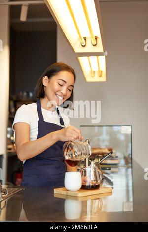 Jolie femme de barista coréenne, en versant du café, en préparant du filtre en lot, en le distribuant, en travaillant dans un café Banque D'Images