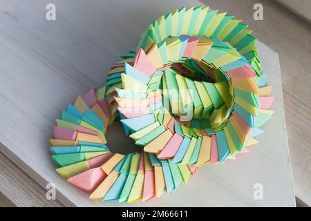 Des anneaux d'origami colorés se trouvent sur une table en bois blanc, structures paramétriques abstraites en feuilles de papier Banque D'Images