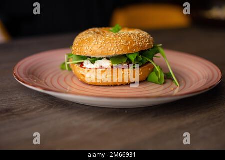 Délicieux hamburger au beignet de sésame avec garniture au fromage et à la végétation, sauce servie sur une assiette rose sur une table en bois Banque D'Images