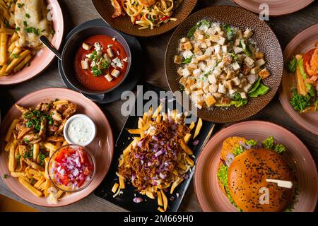 Faites griller les fast-foods sur la table du café. Soupe rouge avec crouton, sauce, hamburger, frites avec pâtes à la viande, sandwich et salade César Banque D'Images