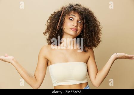 Femme peigne les cheveux bouclés afro avec peigne en bois, produits de coiffage de soins de beauté maison, perte de cheveux après Covid-19, sourire sur fond beige Banque D'Images