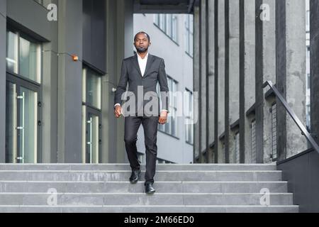 Portrait complet d'un homme d'affaires, un patron afro-américain descend les escaliers à l'extérieur d'un immeuble de bureaux moderne, l'homme se précipite vers le bureau pour le travail. Banque D'Images