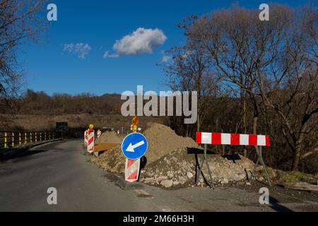 Photo intéressante de travaux routiers sur un petit pont. L'image montre des saletés excavées et de l'asphalte récemment déposé entouré de panneaux d'avertissement et de signaux Banque D'Images