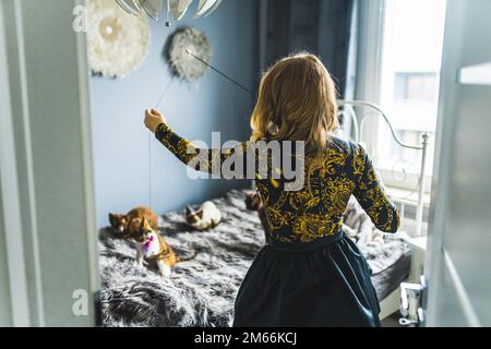 Photo d'une femme blonde jouant avec des chats Devon rex assis sur le lit, prise de derrière. Concept PET. Prise de vue moyenne. Photo de haute qualité Banque D'Images