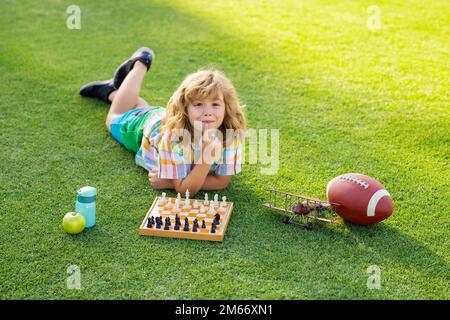 Enfant concentré développer la stratégie d'échecs, jouer à un jeu de société dans l'arrière-cour, poser sur l'herbe. Banque D'Images