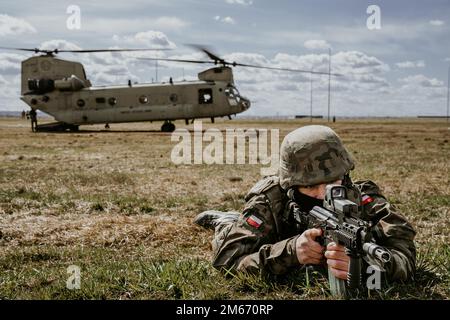 Un soldat des forces armées polonaises scanne son secteur en tant qu'américain L'hélicoptère Chinook de l'armée CH-47 du bataillon de l'aviation générale 1-214th, 12th Brigade de l'aviation de combat, charge du personnel en arrière-plan, lors d'un exercice conjoint mené par les forces armées polonaises dans la zone d'atterrissage près de l'arène G2A, en Pologne, au 8 avril 2022. Cet exercice, ainsi que d'autres, renforce notre interopérabilité avec nos alliés et partenaires de l'OTAN et renforce les relations régionales que nous avons développées. 12 CAB est la seule brigade d'aviation durable présente dans toute l'Europe qui nous permet de dissuader et de défendre aga Banque D'Images