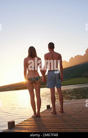 Baigneurs au coucher du soleil. Photo d'un jeune couple en maillots de bain debout sur un quai au coucher du soleil. Banque D'Images