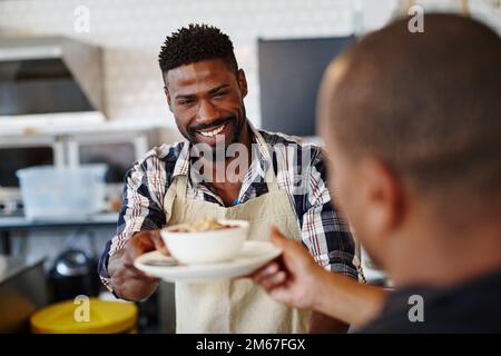 Voilà, monsieur, profitez. un jeune homme servant un client dans un café. Banque D'Images