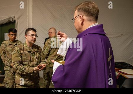L'archevêque lituanien Gintaras Grušas présente le 2nd Lt. Ian bain, officier blindés du 3rd Battalion, 66th Armored Regiment, 1st Armored Brigade combat Team, 1st Infantry Division, avec la Sainte communion lors d'une messe catholique au Camp Herkus, Lituanie, le 12 avril 2022. Résolution atlantique, lutte comme un, les gens d'abord, plus fort ensemble, armée américaine, Banque D'Images