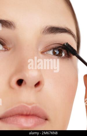Mettant en évidence ses cils. une belle jeune femme appliquant la mascara sur un fond blanc. Banque D'Images