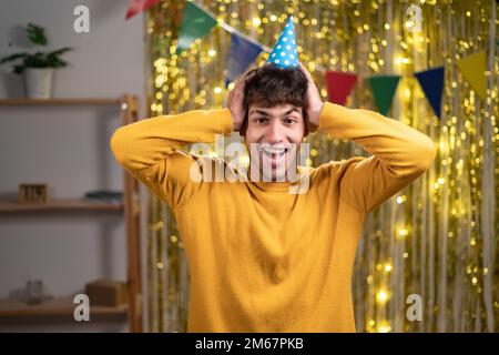 Gros plan photo de l'homme drôle dans l'ambiance festive hatgood écouter les nouvelles positives bouche ouverte bras sur la tête porter décontracté jaune chaud chandail. fête d'anniversaire à la maison Banque D'Images