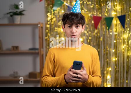 Portrait de l'étonnant gars fou dans le chapeau de fête utiliser le téléphone portable lire de l'information merveilleuse impressionné Scream wow omg, célébrant sa fête d'anniversaire à Banque D'Images