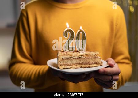 Gâteau avec le numéro 20 bougies allumées dans les mains des hommes. 20th anniversaire Banque D'Images