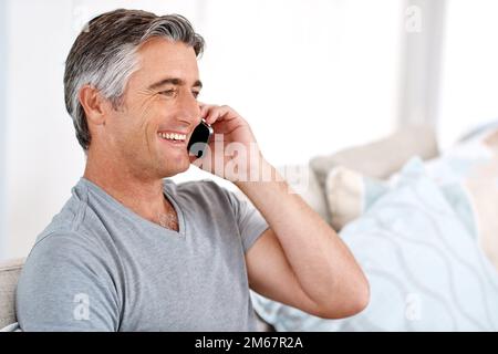 La technologie rend la vie beaucoup plus facile. un beau homme mûr assis sur son canapé de salon seul et parlant sur son téléphone portable. Banque D'Images