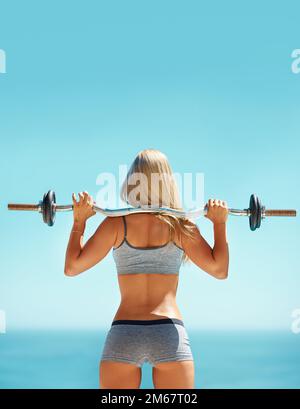 Elle parle grand, mais elle peut l'aider. Vue arrière d'une jeune femme faisant des squats avec une barbelette à l'extérieur. Banque D'Images