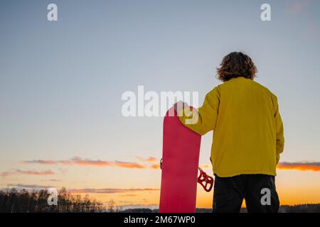 Snowboardeur tenant un snowboard sur le sommet de la montagne et regardant se refléter dans une distance. Vacances d'hiver. Banque D'Images