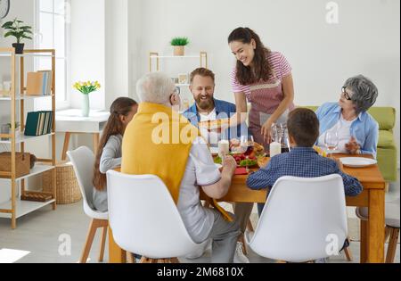 Une femme sert la table pour une grande famille dans la salle à manger avec un sourire sur son visage. Banque D'Images