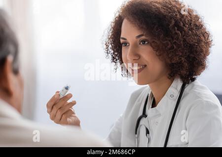 souriant afro-américain médecin tenant lancet stylo dispositif près de l'homme flou, image de stock Banque D'Images
