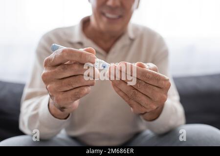 vue rognée d'un homme d'âge moyen souriant prenant un échantillon de sang avec un stylo à lancette, image de stock Banque D'Images