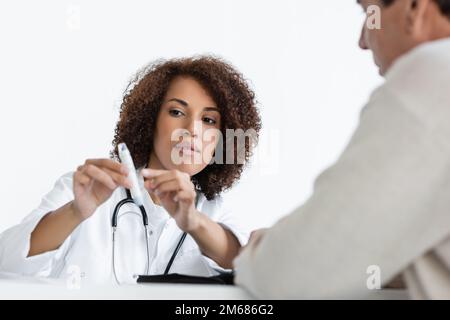 jeune afro-américain médecin pointant avec le doigt sur le stylo lancet près de flou de l'âge moyen patient avec le diabète dans la clinique, image de stock Banque D'Images