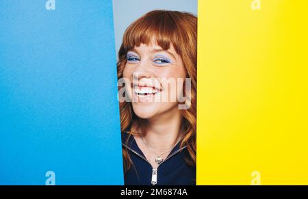 Bonne femme debout avec deux formes de design colorées. Femme aux cheveux de gingembre s'amusant dans un studio d'art. Banque D'Images