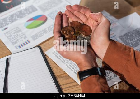 KIEV, UKRAINE - 17 NOVEMBRE 2022 : vue rognée d'un homme d'affaires avec une poignée de bitcoins près du bureau avec des documents Banque D'Images