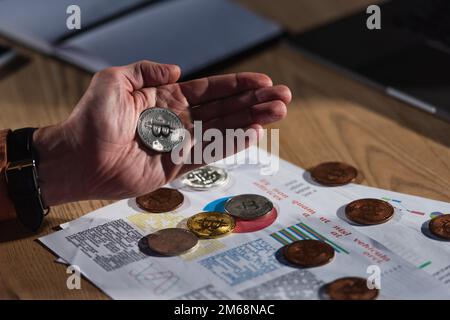 KIEV, UKRAINE - 17 NOVEMBRE 2022 : bitcoin d'argent en main de l'homme de culture près de papiers avec analyse d'affaires Banque D'Images