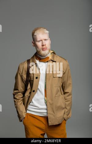 albinos barbu dans une élégante veste de chemise et un foulard en soie debout avec les mains dans les poches isolées sur gris, image de stock Banque D'Images