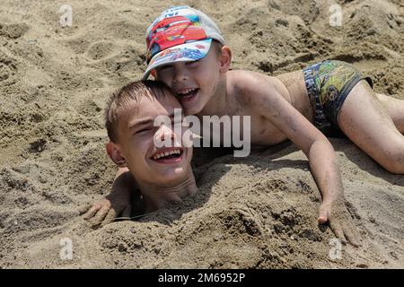 Lac Uvildy, région de Chelyabinsk, Russie - 09 juillet 2019. Deux garçons sont couchés sur la rive du lac, l'un d'eux est enterré jusqu'à son cou dans le sable Banque D'Images