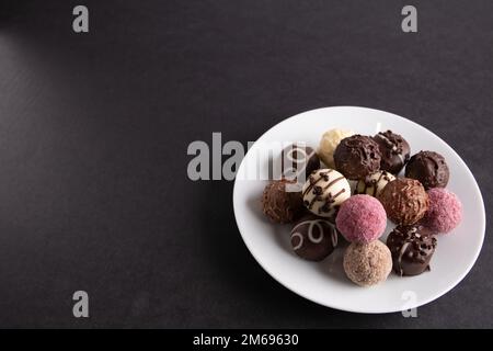 photochez différents chocolats dans une assiette sur fond noir Banque D'Images