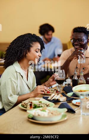 Une femme mange son dîner dans un restaurant tout en étant assise à la table avec ses amis. Banque D'Images