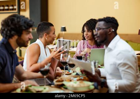 Des hommes d'affaires très occupés s'assoient à la table du dîner dans un restaurant, travaillent sur des ordinateurs portables et ont une réunion importante. Banque D'Images