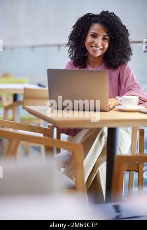 Un freelancer hispanique se présente sur l'ordinateur portable et sourit à la caméra tout en étant assis dans le café. Banque D'Images