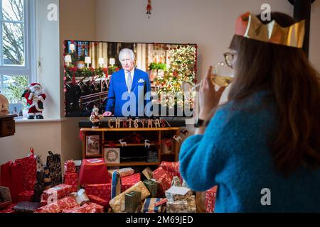 Lors de sa première émission du jour de Noël au pays depuis la mort de sa mère, la reine Elizabeth III en septembre, le roi Charles III parle à une famille de banlieue sur leur téléviseur grand écran dans leur salon rempli de cadeaux enveloppés, le 25th décembre 2022, à Nailsea, en Angleterre. Banque D'Images