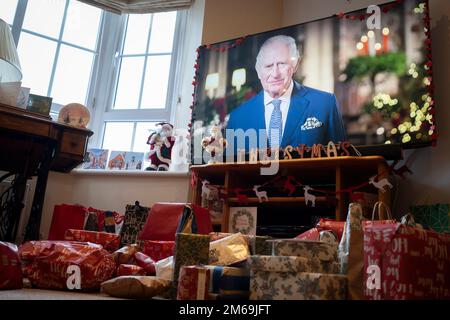 Lors de sa première émission du jour de Noël au pays depuis la mort de sa mère, la reine Elizabeth III en septembre, le roi Charles III parle à une famille de banlieue sur leur téléviseur grand écran dans leur salon rempli de cadeaux enveloppés, le 25th décembre 2022, à Nailsea, en Angleterre. Banque D'Images