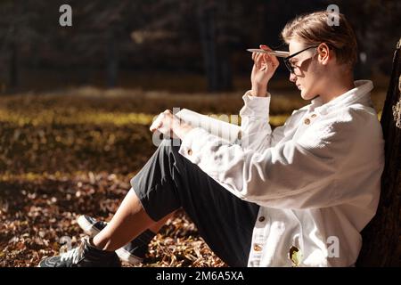 Femme assise au sol dans le parc avec un journal sur ses genoux et pensant à des notes dans le carnet. Banque D'Images