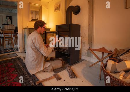 Homme commençant cheminée dans Old Cottage House poêle à bois Banque D'Images