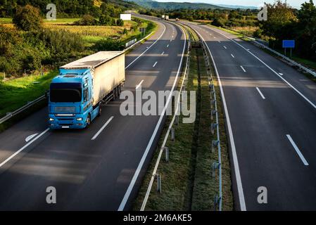 Grand semi-camion industriel bleu pour livraison de fret commercial long-courrier avec semi-remorque avançant le long de la route Banque D'Images