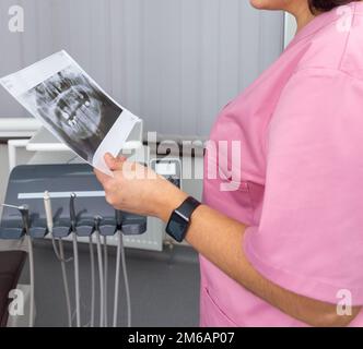 Femme dentiste en uniforme rose regardant le roentgen de la mâchoire humaine. Conseil. Femme dantist tenant des dents X-ray photographie. Banque D'Images